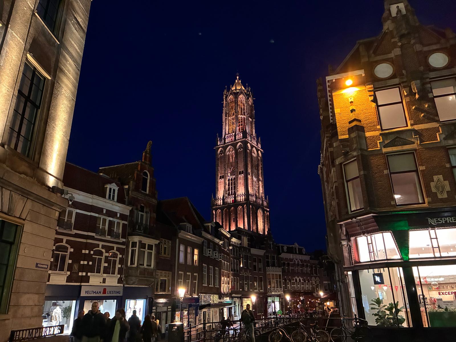 The illuminated Gothic Dom Tower of Utrecht rising above historic canal houses at night with warm street lights