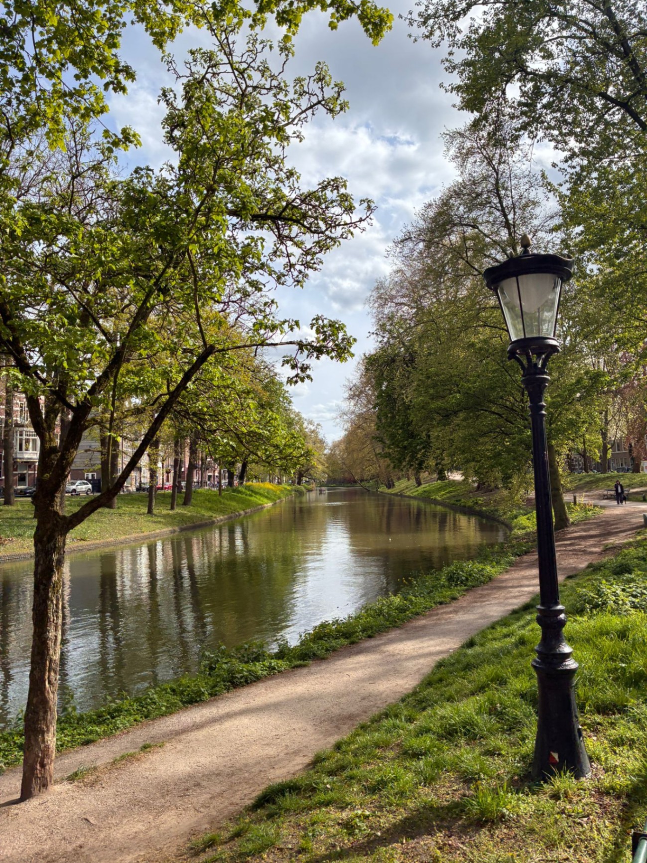 Quiet tree-lined Singel canal in Utrecht in spring with a classic black lantern, footpath and green reflections in the water